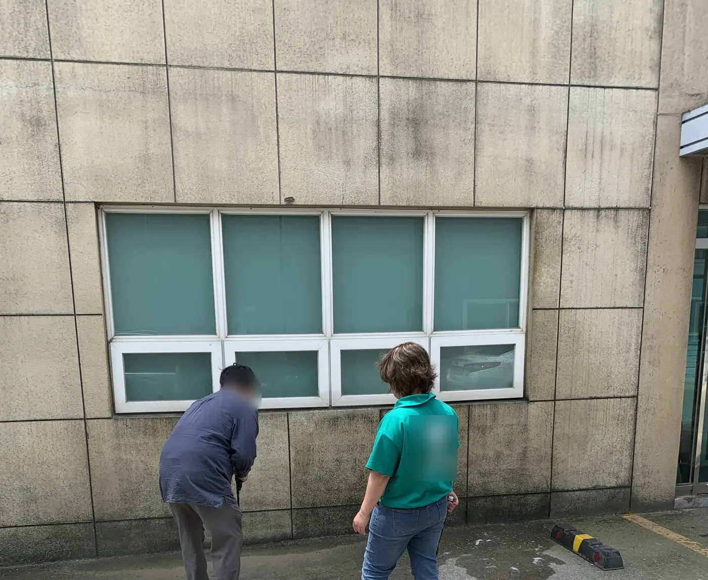 창 아래 하단 석재 띠 앞에서 이동식 고압세척기로 벽을 씻는 작업 모습