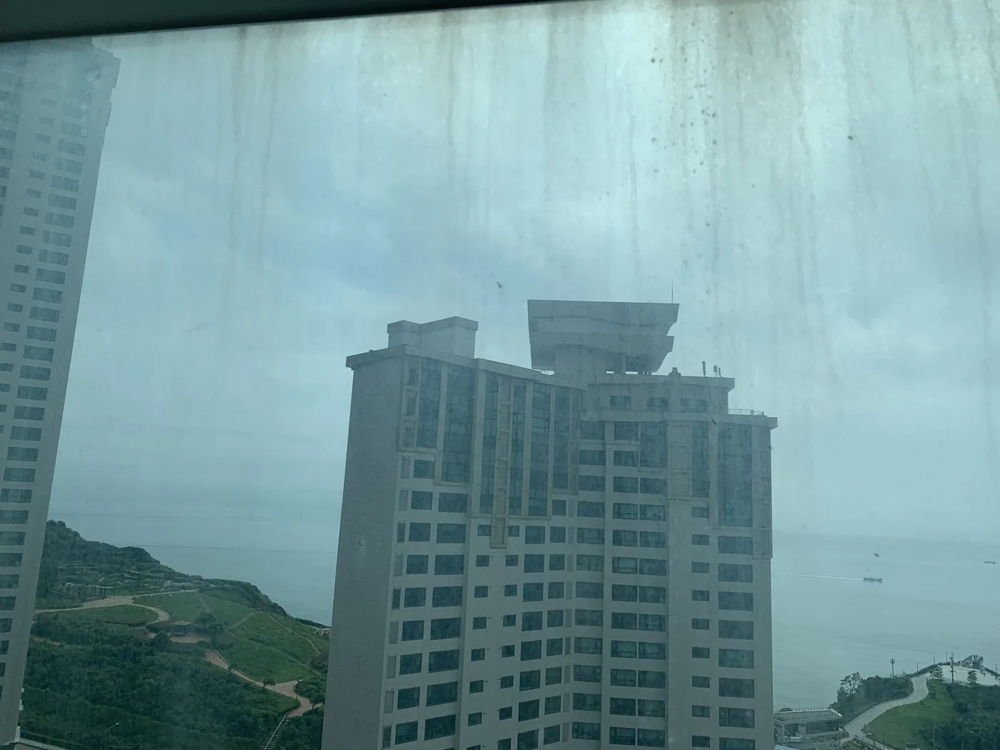부산 고층 아파트 통창 유리에 빗물 자국과 먼지가 얼룩진 작업 전 모습, 창밖으로 건너편 고층 건물이 보인다