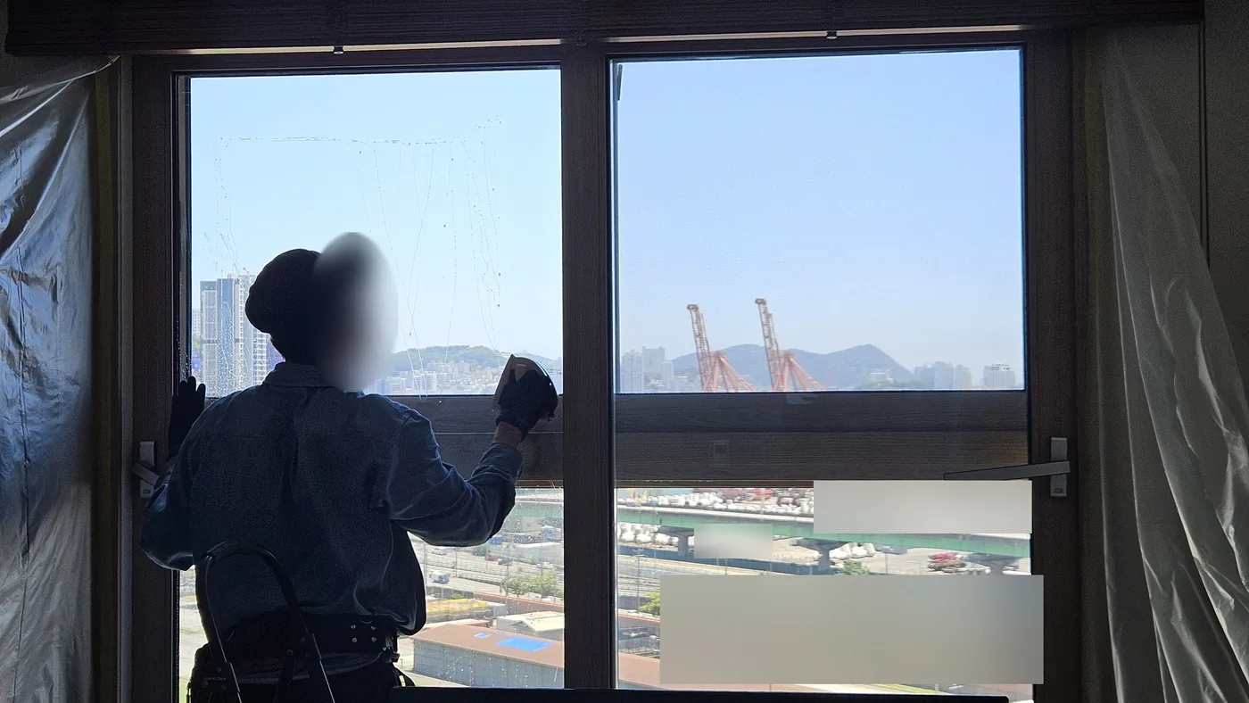 부산 동구 고층 아파트 방 창 앞에서 모자와 마스크를 쓴 작업자가 장갑 낀 손으로 윗칸 유리를 닦는 모습