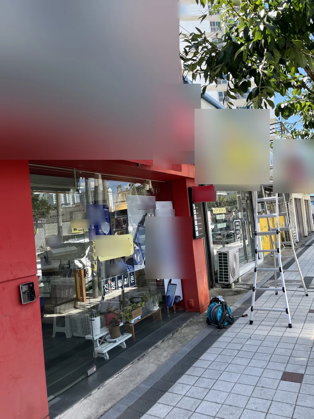 영천 휴대폰 매장 전면의 빨간 프레임과 유리, 그 위에 접힌 어닝 덮개와 인도에 세워 둔 사다리