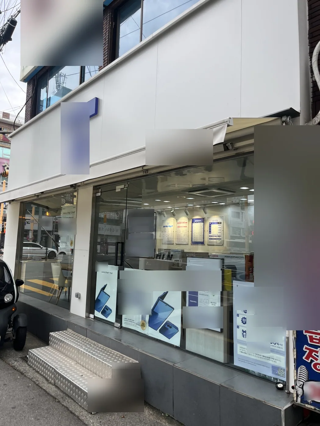 울산 중구 휴대폰 매장 옆면의 흰 판넬과 접힌 어닝, 긴 유리창