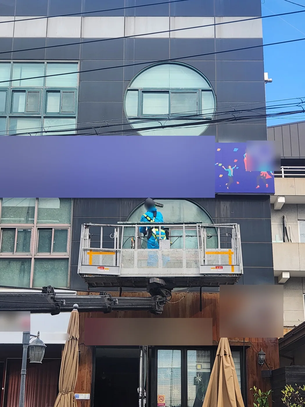 간판과 1층 매장 사이 둥근 창 앞에 바스켓을 대고 창을 닦는 작업자