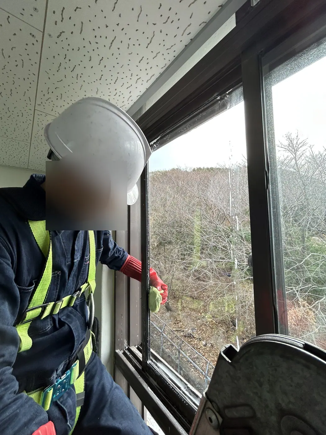 부산 서구 전시시설에서 안전모와 안전대를 갖춘 작업자가 천장 가까이 달린 창의 틀을 천으로 닦는 모습