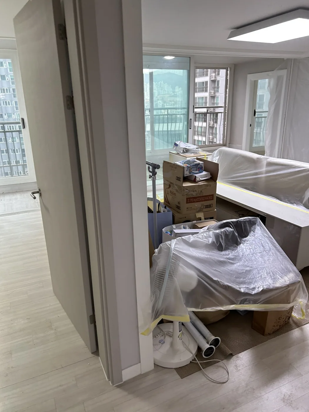 부산 해운대 아파트 거실에 비닐로 덮어 둔 가구와 쌓아 둔 상자, 그 너머의 난간 쪽 창