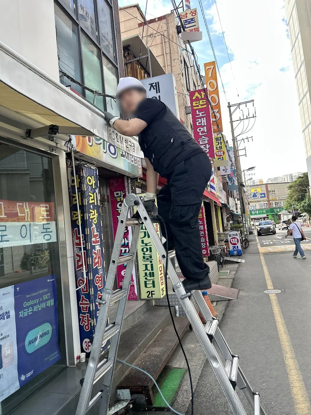 울산 중구 통신매장 앞에서 헬멧을 쓴 작업자가 사다리 위에서 어닝 프레임을 닦는 모습