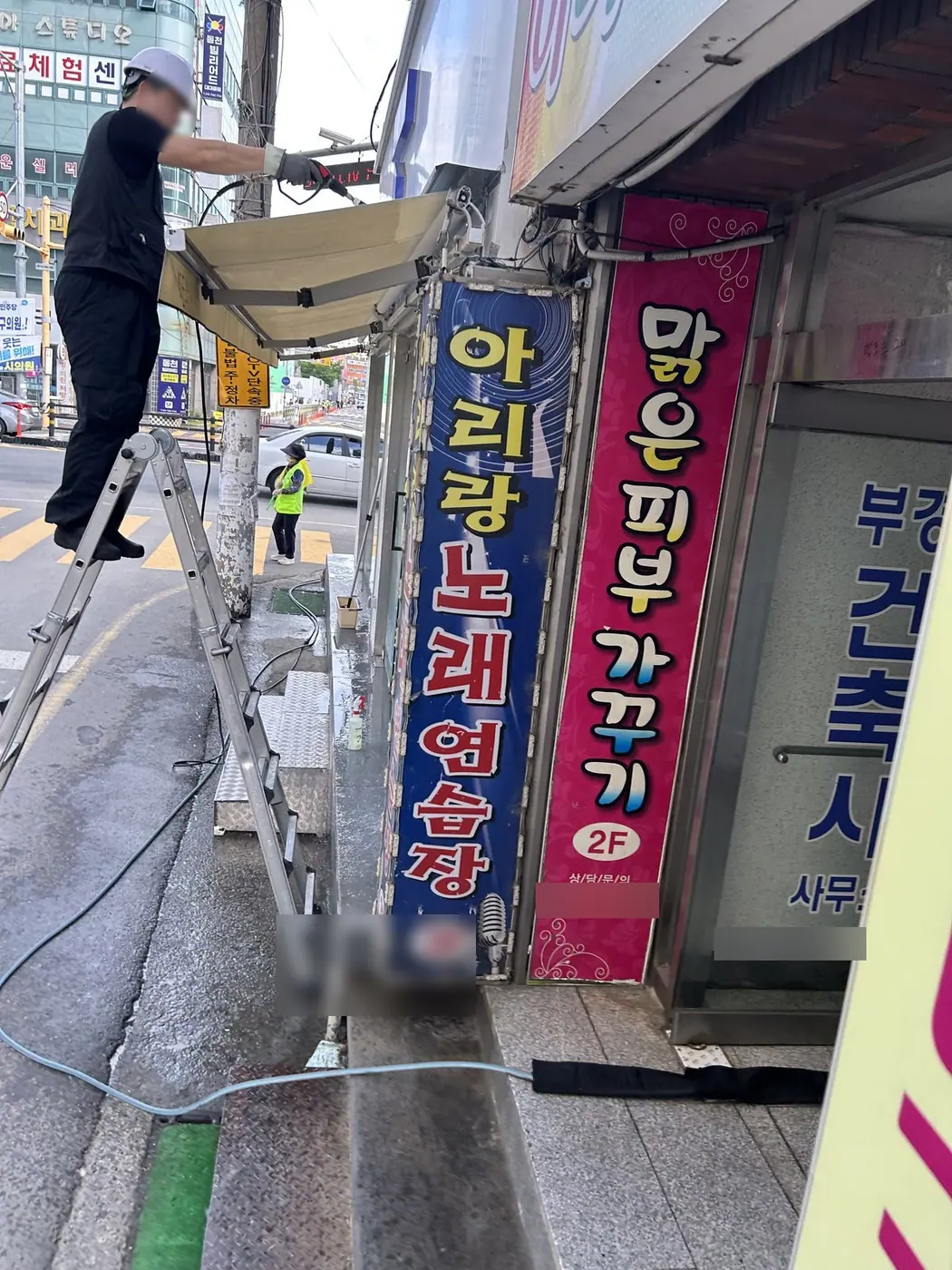 사다리 위의 작업자가 어닝 끝단을 잡고 천의 먼지를 닦는 모습