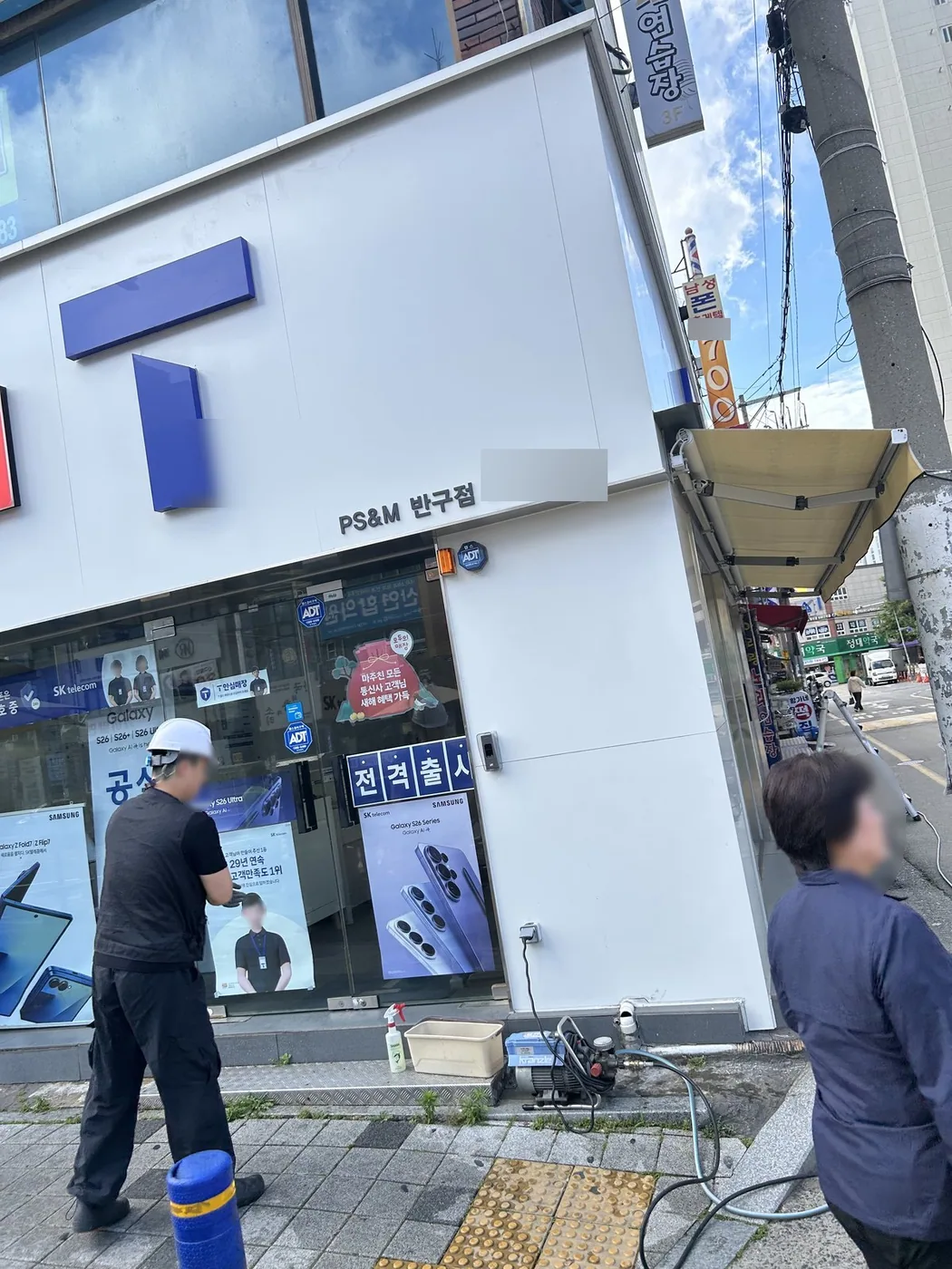 헬멧을 쓴 작업자가 매장 앞에서 저압 세척기와 호스를 정리하는 모습