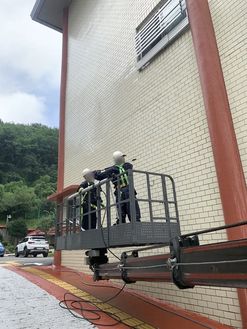 도로에서 올려다본 건물 외벽에 고소작업대 바스켓이 올라가 있는 장면