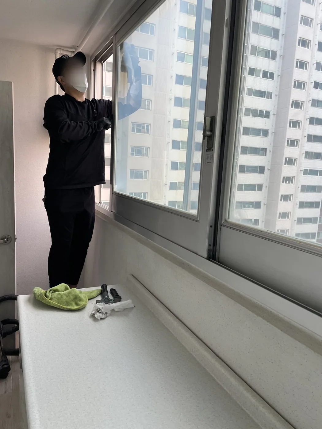 베란다 창 앞에 선 작업자가 유리면을 도구로 세척하는 장면