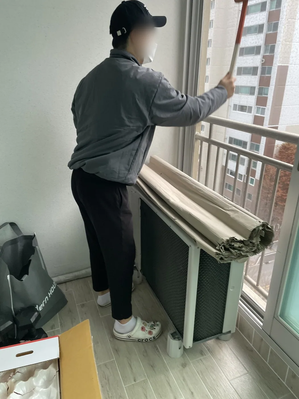 작업자가 베란다에서 발판에 올라 창 상부 구간을 세척하는 장면