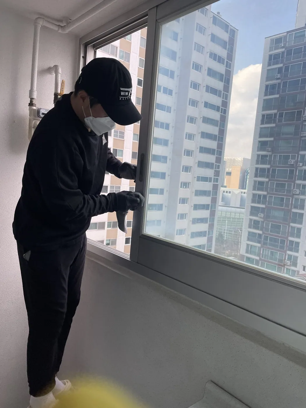 작업자가 베란다 이중창의 창짝 면을 손으로 닦는 장면