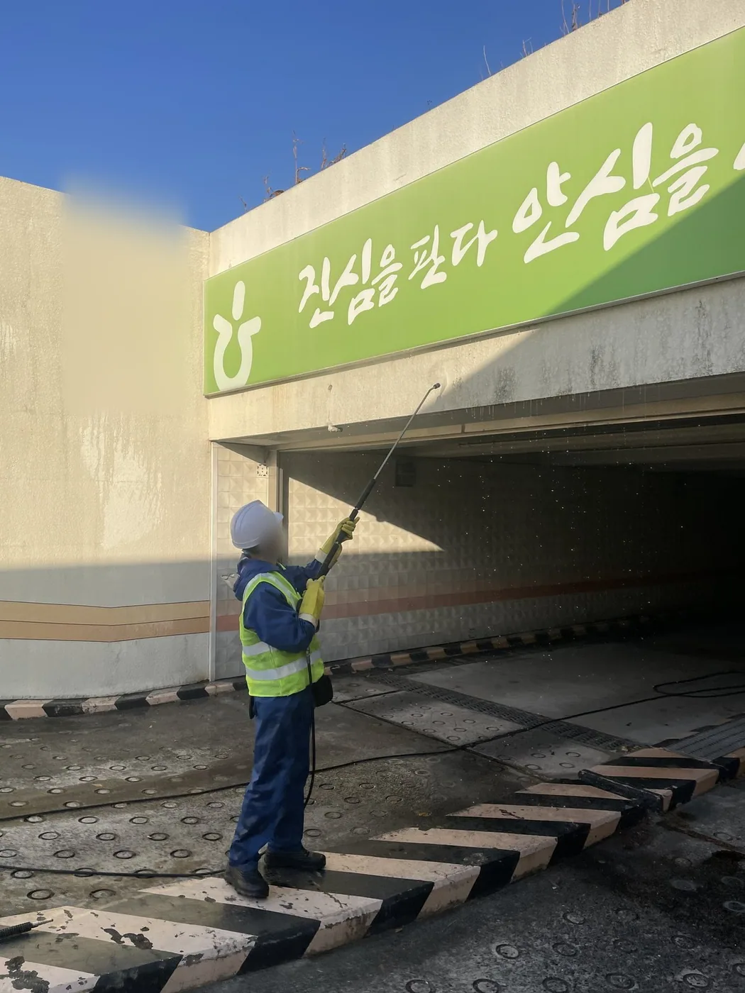 경사진 진입로 위쪽 벽면을 향해 작업자가 폴대를 세워 분사하는 장면