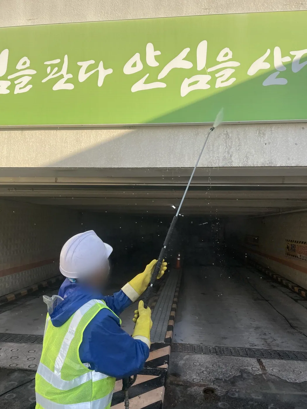 작업자가 긴 폴대 장비를 잡고 개구부 안쪽 벽면을 세척하는 근접 장면