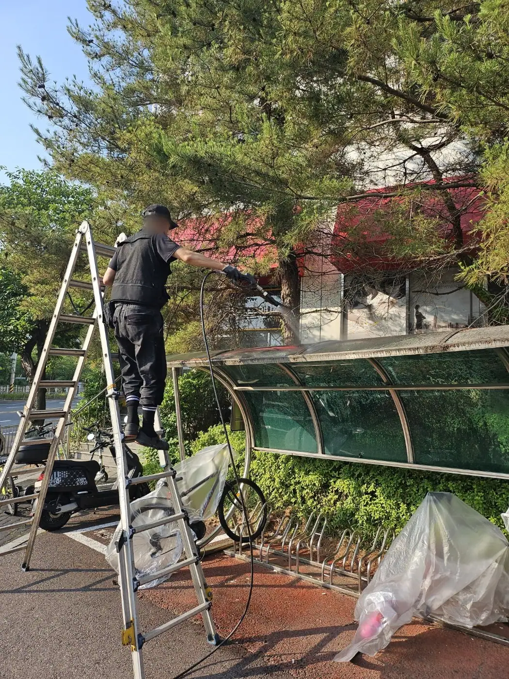 자전거 거치대 위쪽에서 사다리를 세우고 지붕을 세척하는 장면