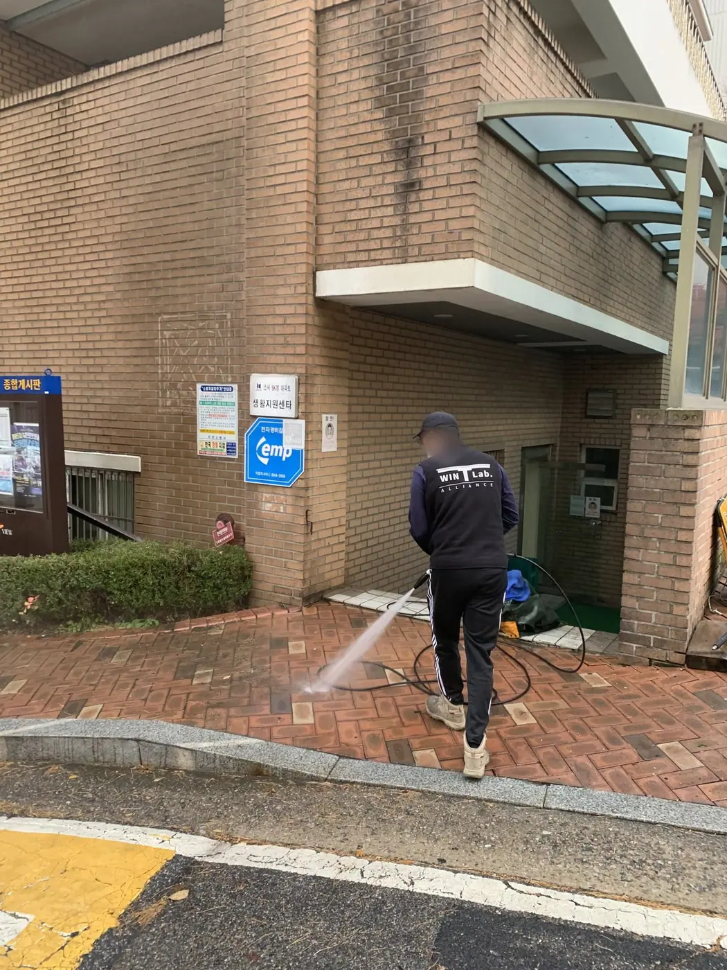 벽돌 건물 출입구 앞 벽면과 바닥을 재료에 맞춰 세척하는 장면
