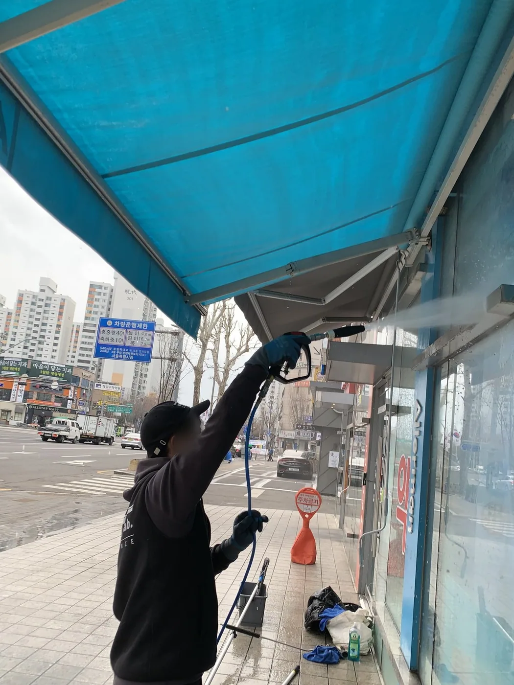 작업자가 파란 원단 어닝 아래에서 안쪽 면을 세척하는 장면