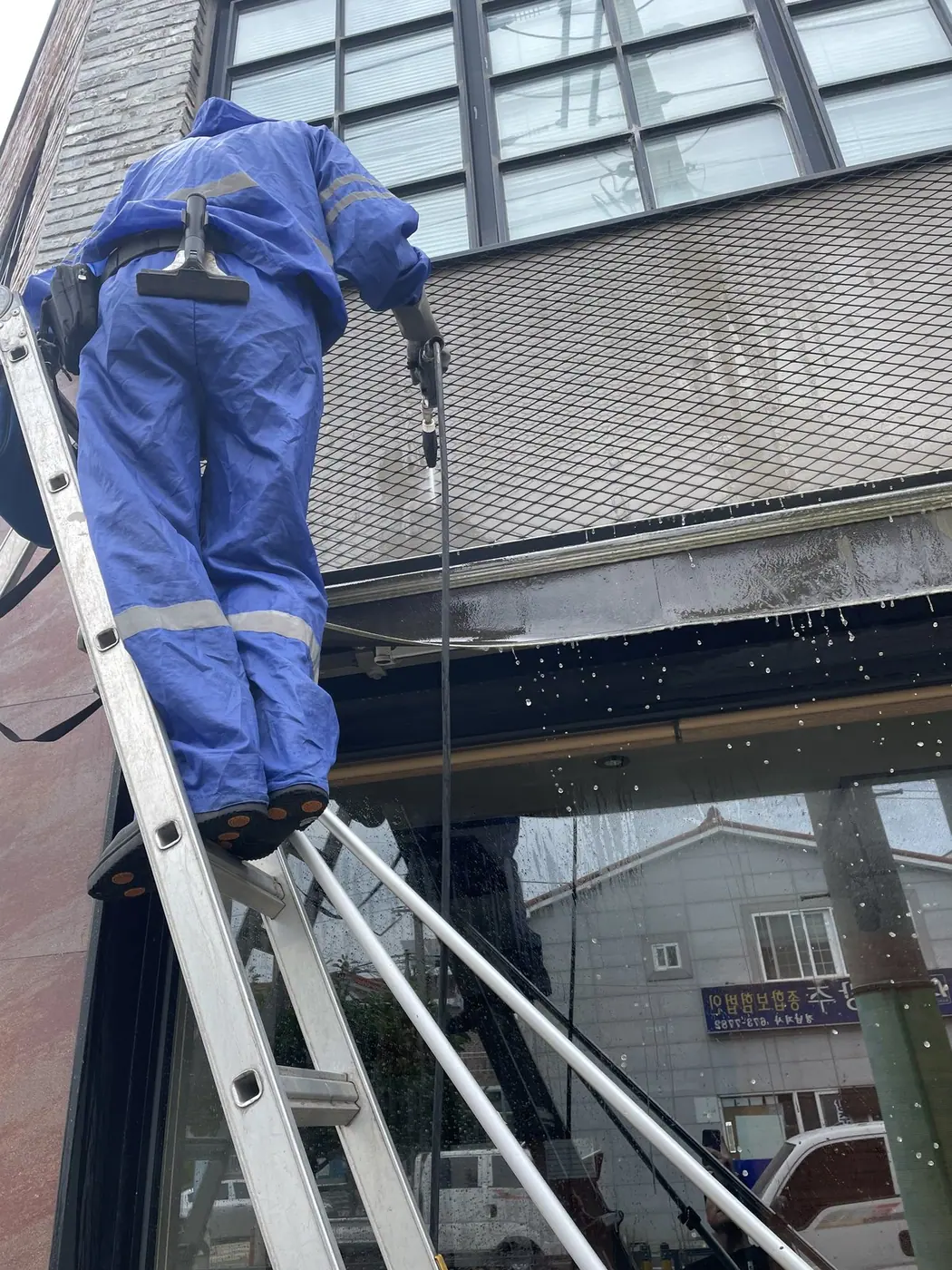 사다리 위 작업자가 검은 캐노피 아래에서 위를 향해 안쪽 면을 세척하는 장면
