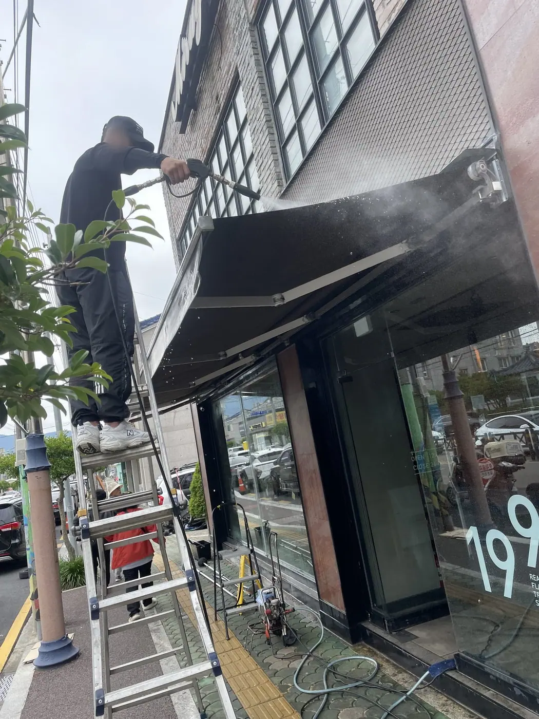 출입구 위 어닝에 물을 분사하며 아래 동선을 비워 둔 장면