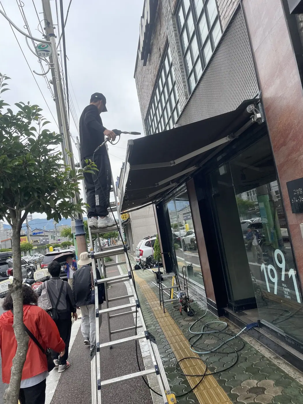 사다리 위에서 검은 캐노피의 프레임 선을 따라 닦는 장면