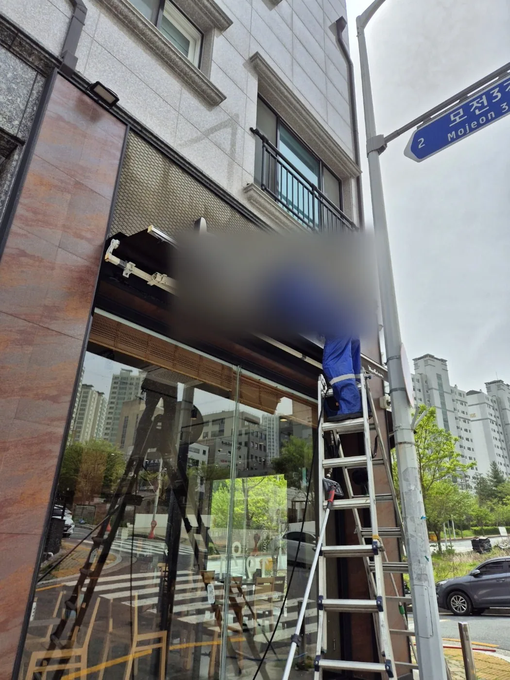유리면에 반사된 사다리와 함께 캐노피 하부를 작업하는 장면
