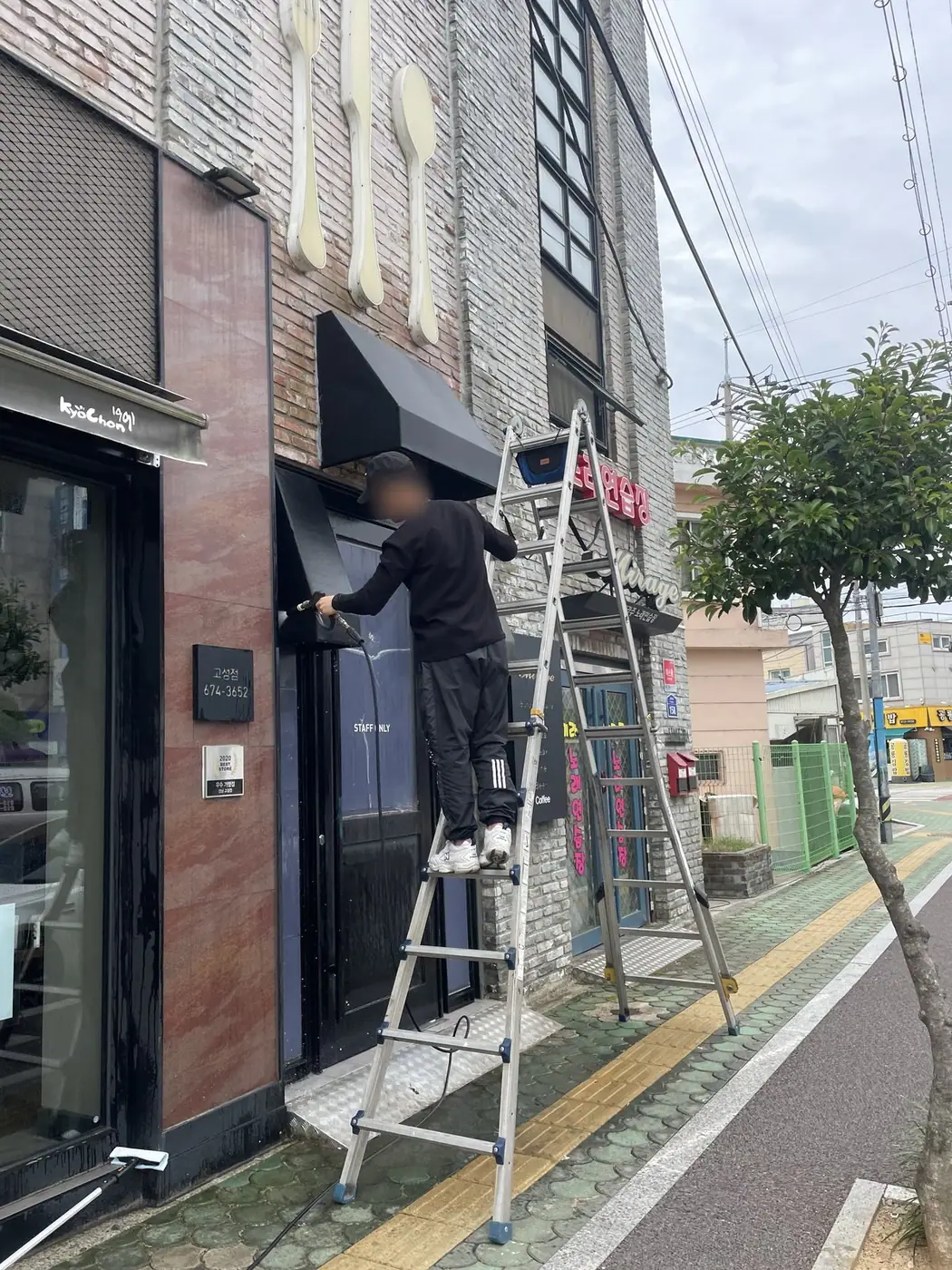보도에서 작업자가 사다리에 올라 어닝 마무리 작업을 하는 장면