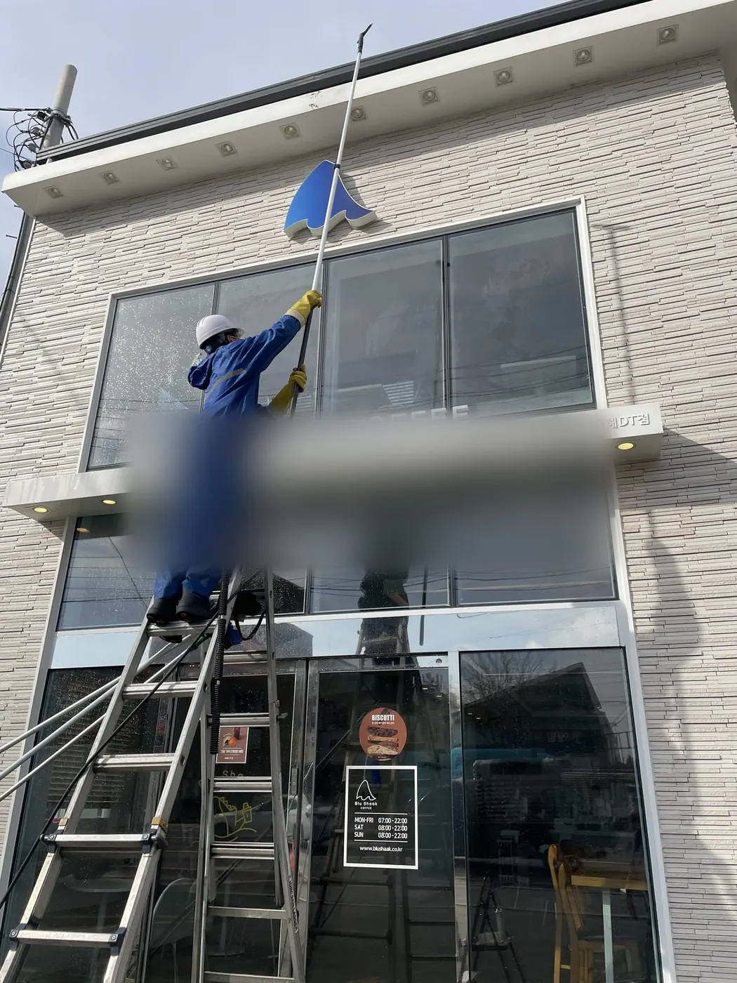점포 측면에서 작업자가 사다리에 올라 유리 구간을 마무리하는 장면
