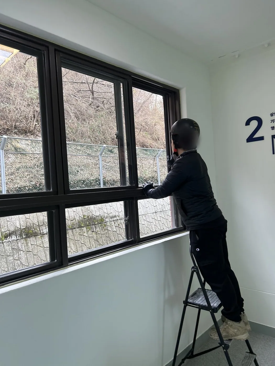 작업자가 발판에 올라 창 상단 가장자리를 손으로 마감하는 장면