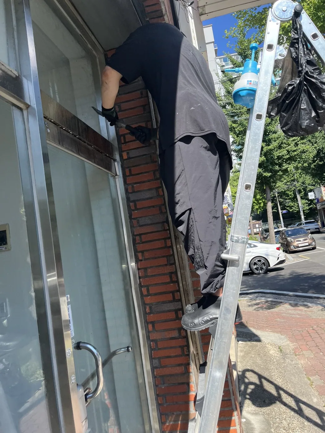 사다리에 올라선 작업자가 상가 창의 상부 구간에 손을 뻗어 작업하는 장면