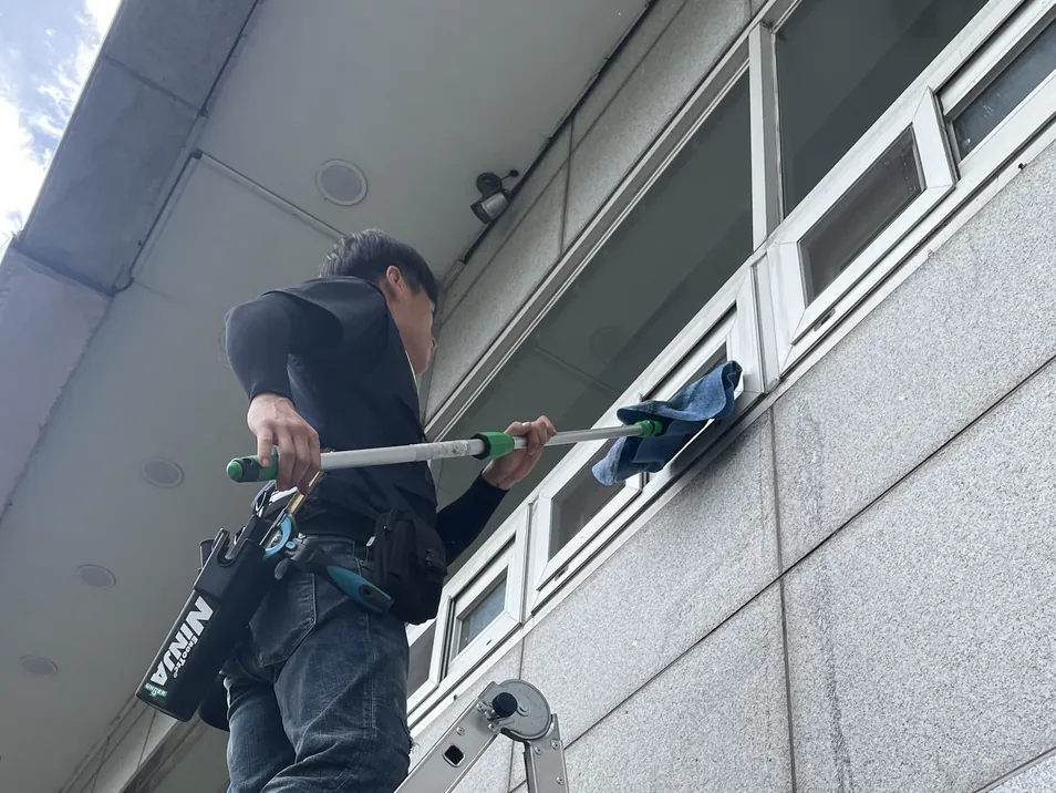 사다리에 올라 매장 외벽 창틀을 닦는 작업자