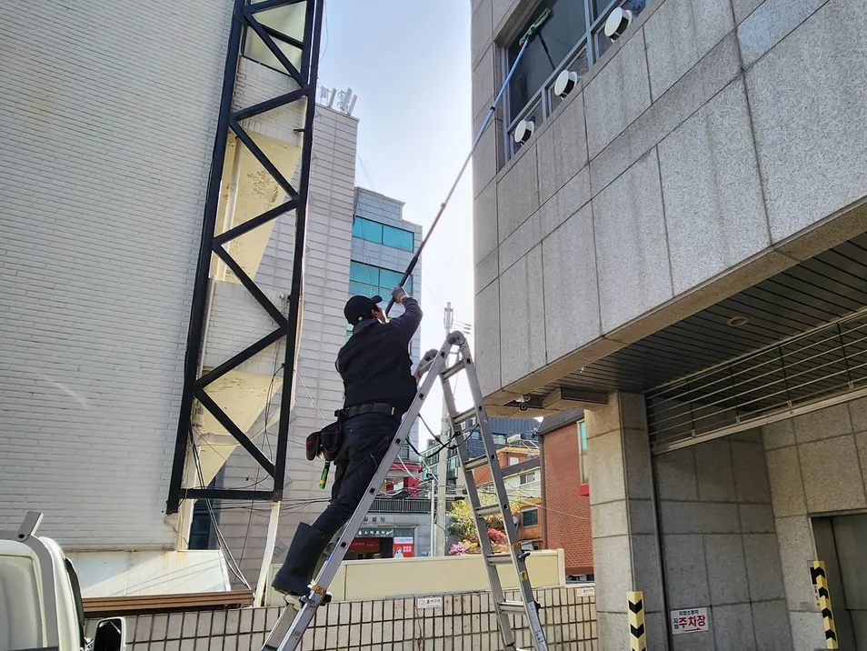 사다리를 세우고 건물 외벽 상단을 고압세척하는 작업자