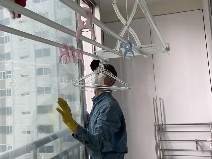 아파트 베란다 창유리를 장갑 낀 손으로 닦는 작업자