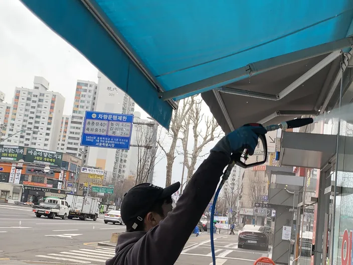 매장 어닝 아래 유리면을 고압 건으로 세척하는 작업자