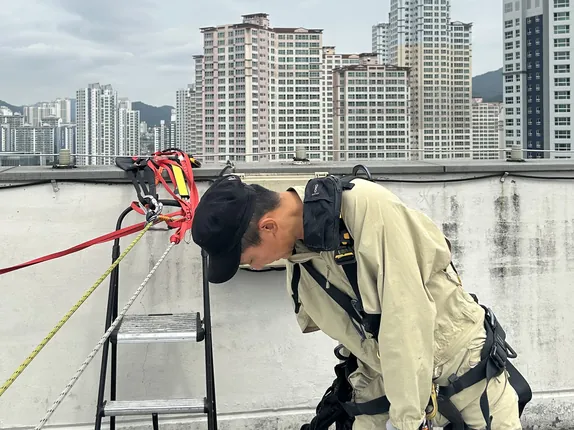 옥상 난간 앞에서 하네스를 착용하는 작업자