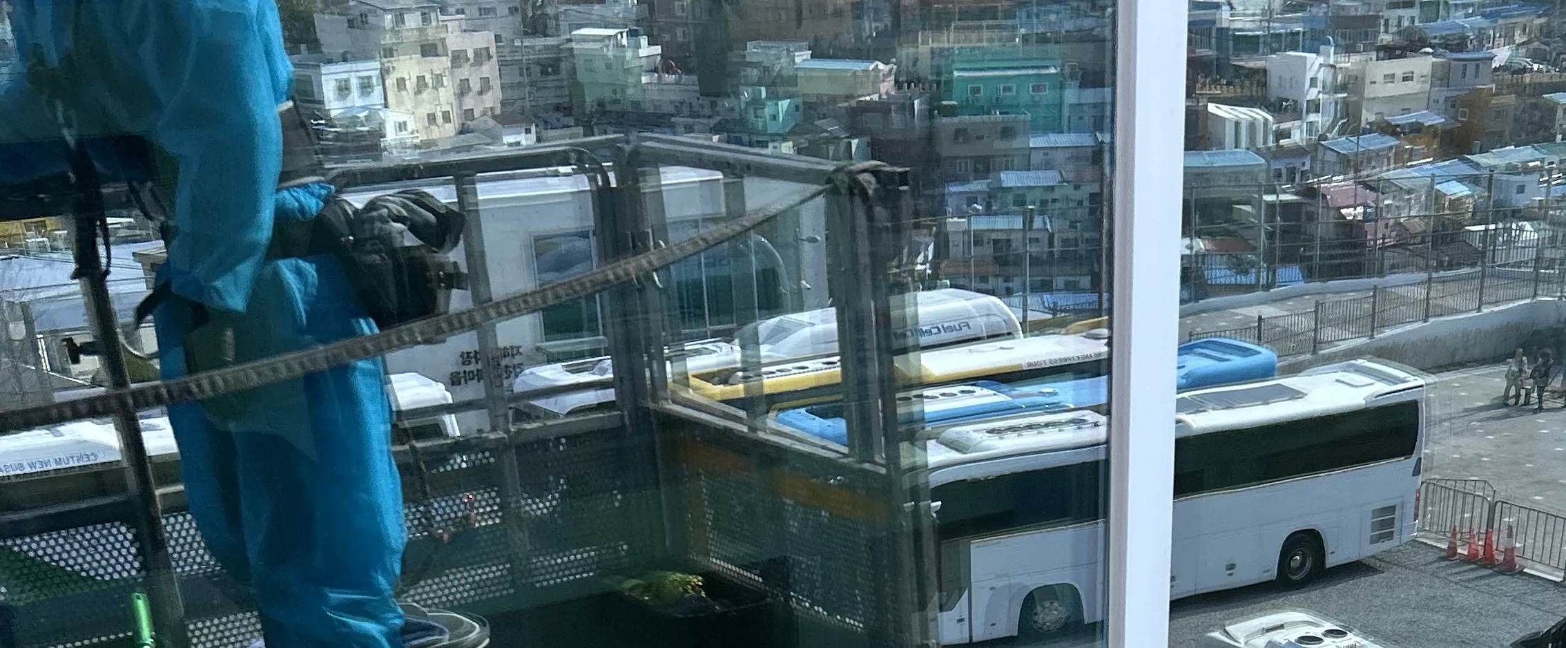빨간 안전모를 쓰고 옥상 유리 난간 바깥면을 닦는 작업자