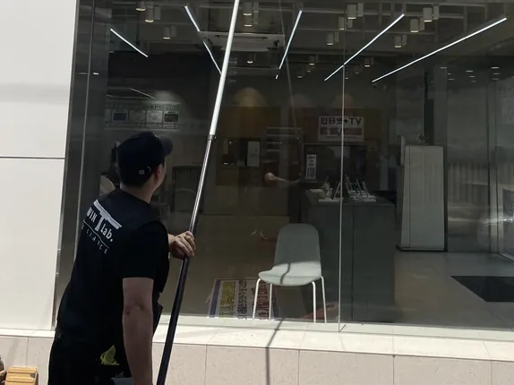 긴 폴대로 매장 통유리를 닦는 작업자