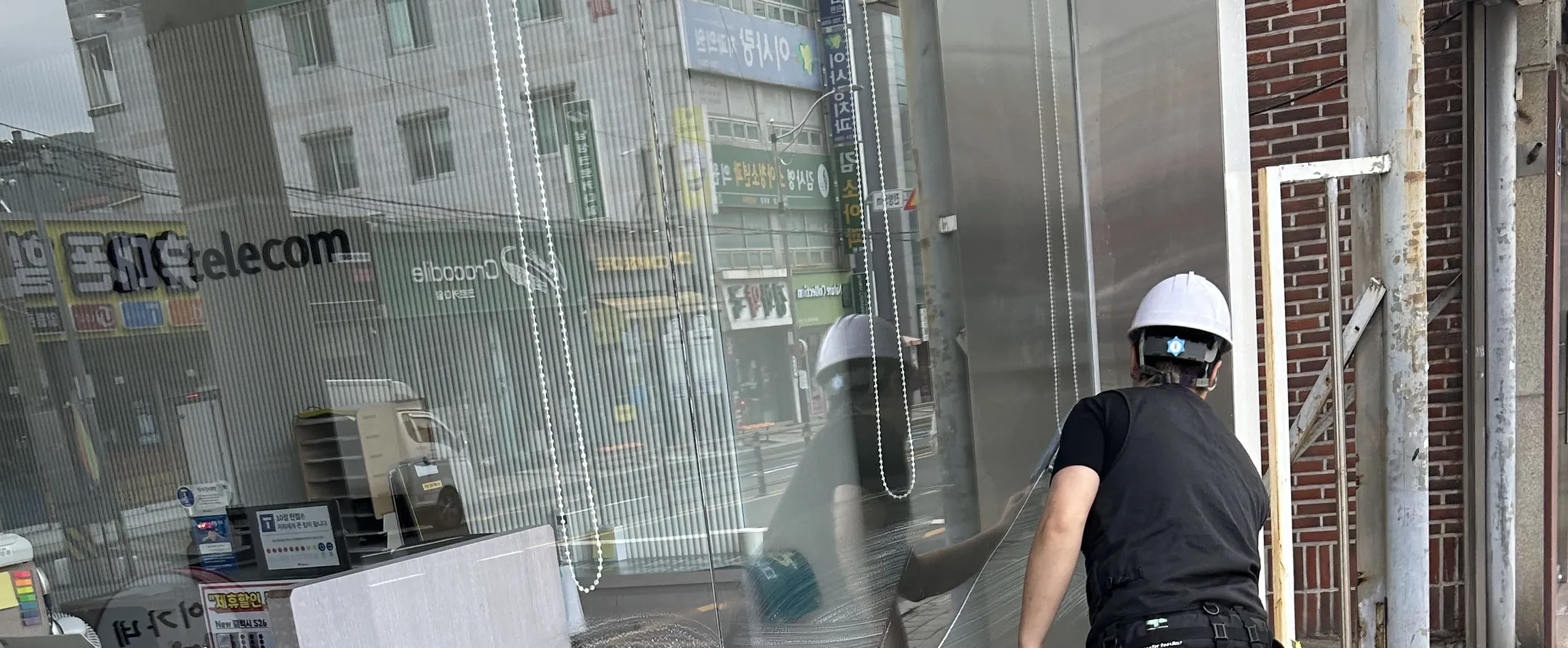 흰 안전모를 쓰고 매장 통유리에 세제 거품을 내어 닦는 작업자